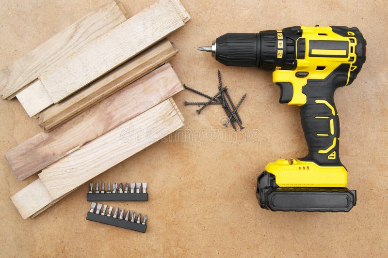 Yellow-black screwdriver on wood background, screws, a set of bits.