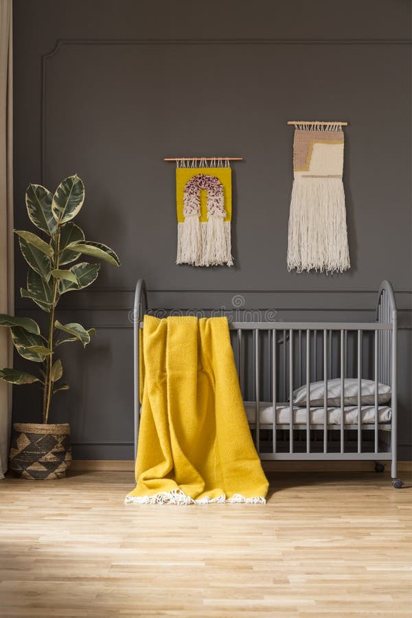 Yellow blanket on baby`s bed in grey bedroom interior with ficus