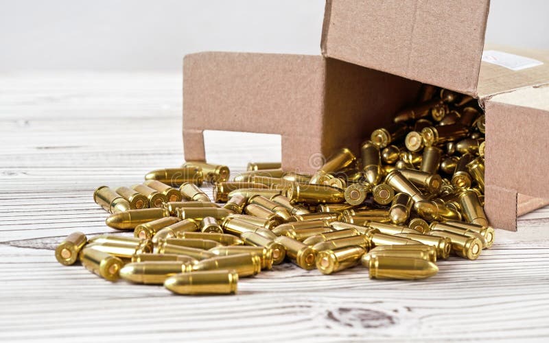 Yellow brass gun ammo spilled from paper carton box on white boar desk - close up stock photo Yellow brass gun ammo spilled from paper carton box on white boar desk - close up stock photo