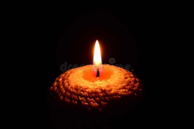 Photo of a yellow candle with a wavy pattern burning on a black background. Photo of a yellow candle with a wavy pattern burning on a black background.