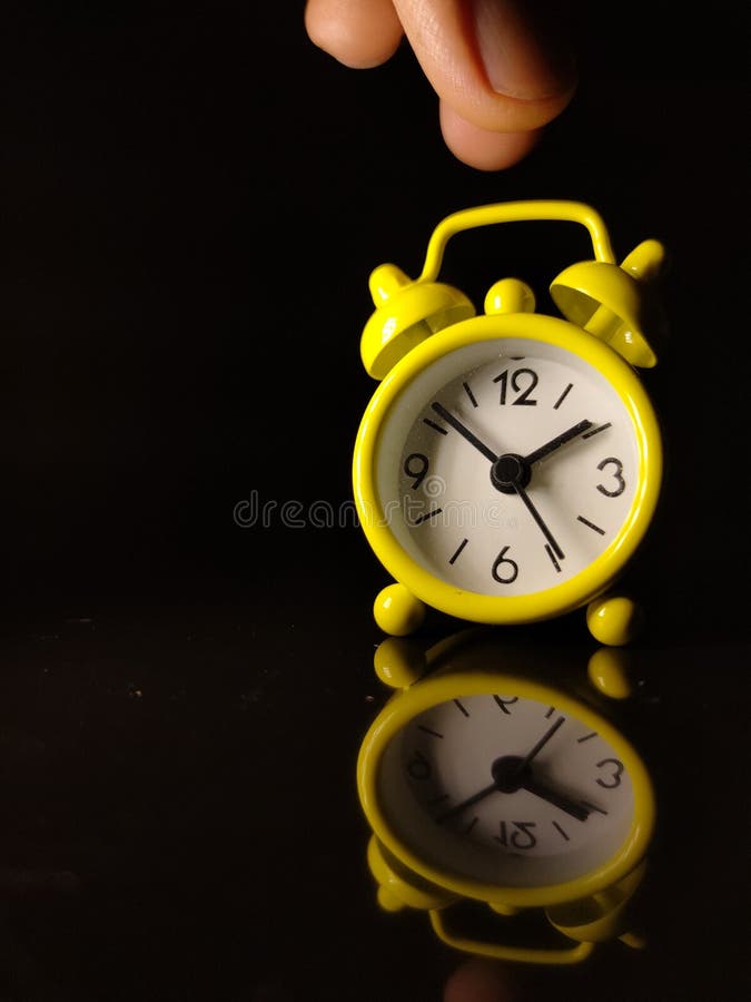 A Yellow Clock with Someone Hand with Reflection on a Black Background