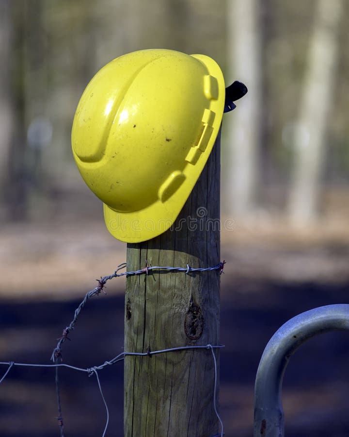 A Yellow Construction Workers Helmet Next To a Fence and Barbed Wire