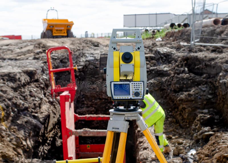 Yellow equipment set out on tripod on building site against cloudless blue sky. Construction site surveying engineering equipment