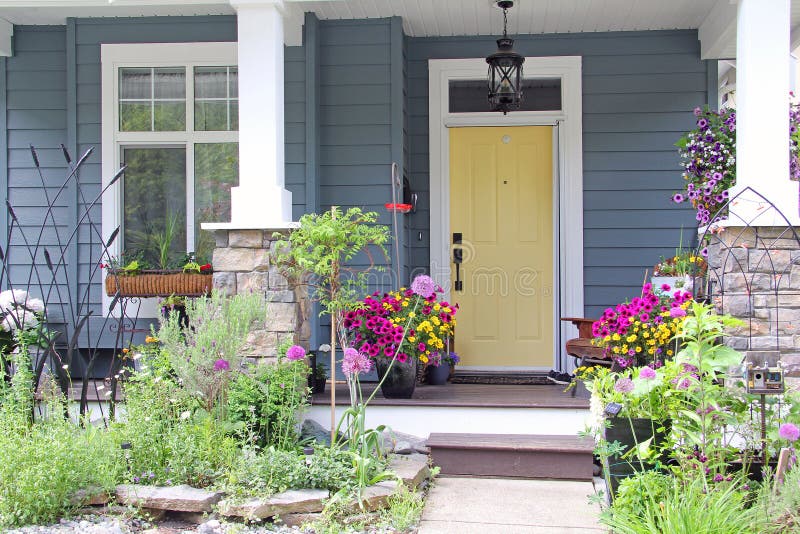 Yellow front door of a small house in the suburbs of Canada. Attractive and colorful front porch surrounded by perennial and annual flowers in summer