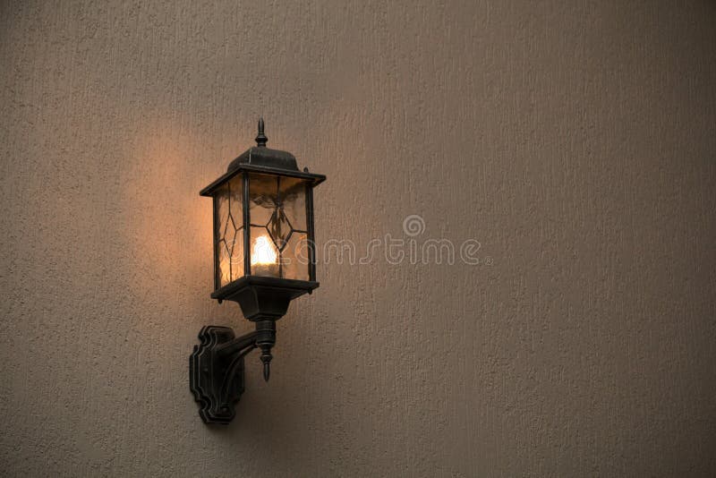 A yellow glass lantern hanging on a gray old wall. Bright glowing lantern illuminating the wall of an ancient building