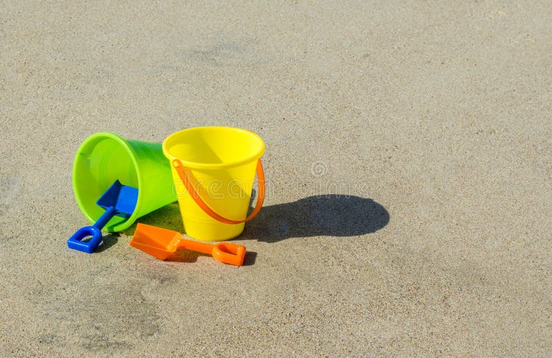 2 plastic sand pails and shovels on a smooth sandy beach