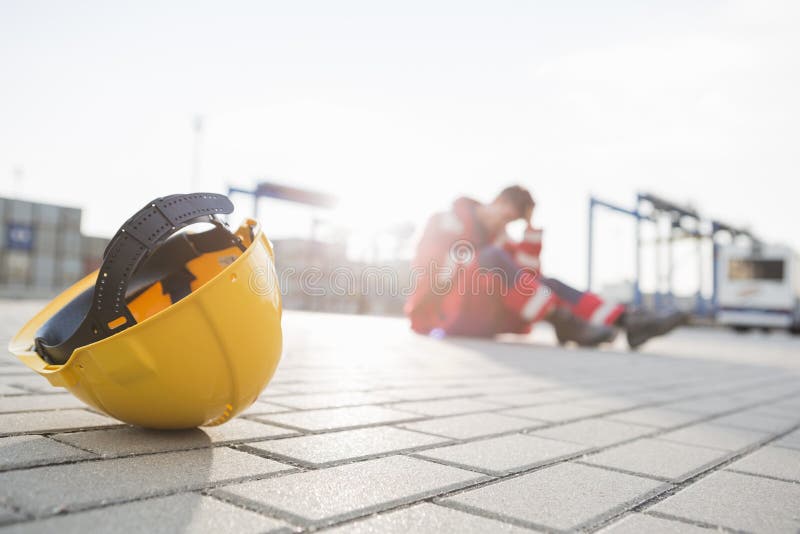 Yellow hardhat at shipyard with depressed male worker in background stock image Yellow hardhat at shipyard with depressed male worker in background stock image