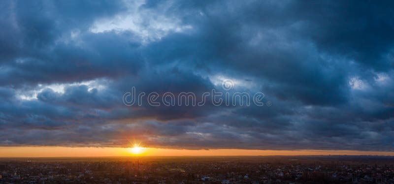 Yellow line of sunset and puffy heavy clouds in the sky over a small town stock photography