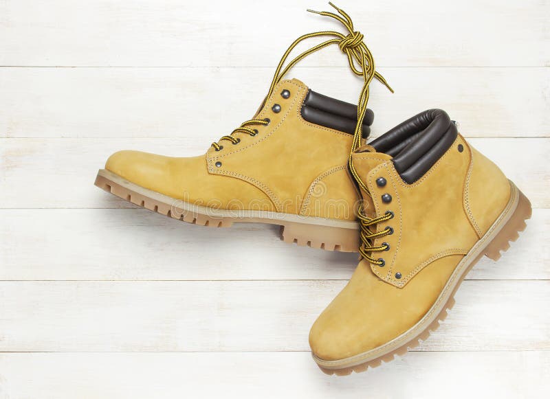 Yellow men`s work boots from natural nubuck leather on wooden white background top view flat lay with copy space. Trendy casual