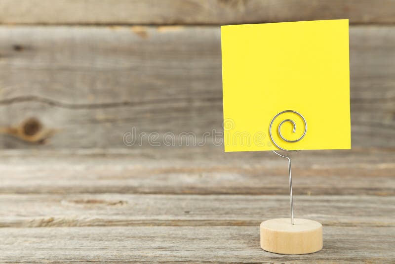 Yellow note paper on a holder on grey wooden background.