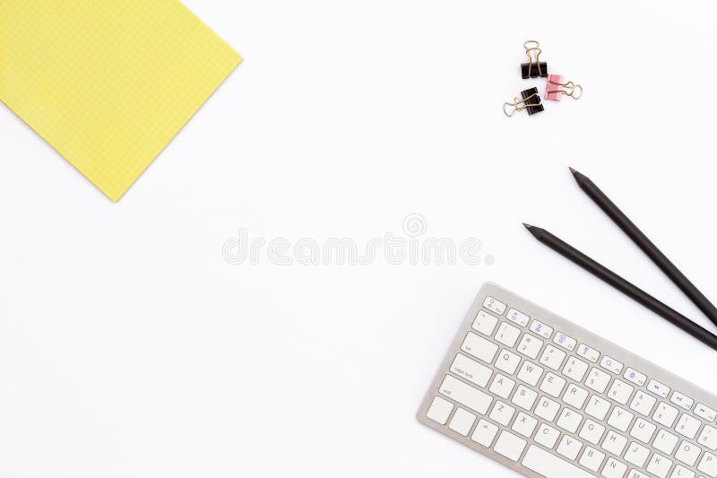 Yellow Notepad, computer keyboard, two black pencil and clips for paper on white background. minimal concept of desktop in the off