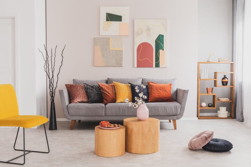 Yellow, orange, black and brown pillows on comfortable grey scandinavian sofa in bright living room interior with abstract