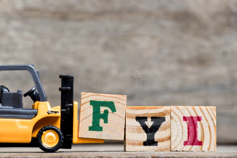 Yellow plastic forklift hold letter F to complete word FYI Abbreviation of For your information on wood background