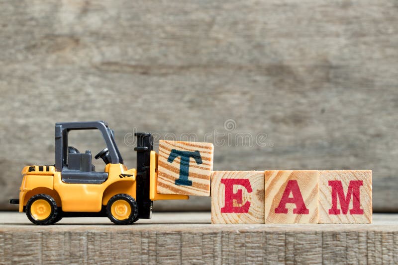Yellow plastic forklift hold letter T to complete word TEAM on wood background