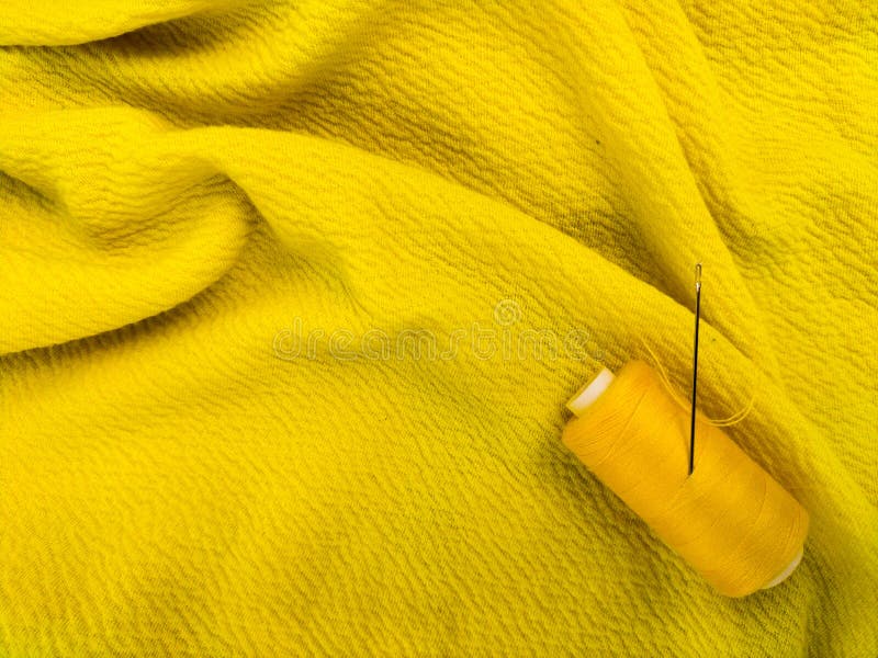 A yellow sewing thread spool lies on a textured yellow fabric royalty free stock images