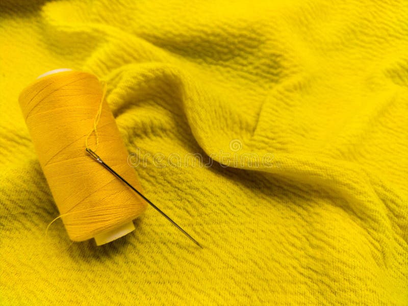 A yellow sewing thread spool lies on a textured yellow fabric royalty free stock photos
