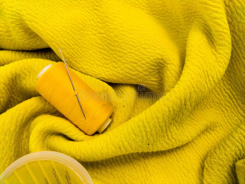 A yellow sewing thread spool lies on a textured yellow fabric royalty free stock photography