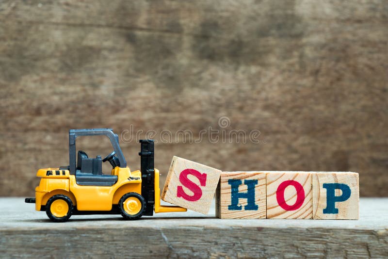 Yellow toy forklift hold letter block S to complete word shop on wood background