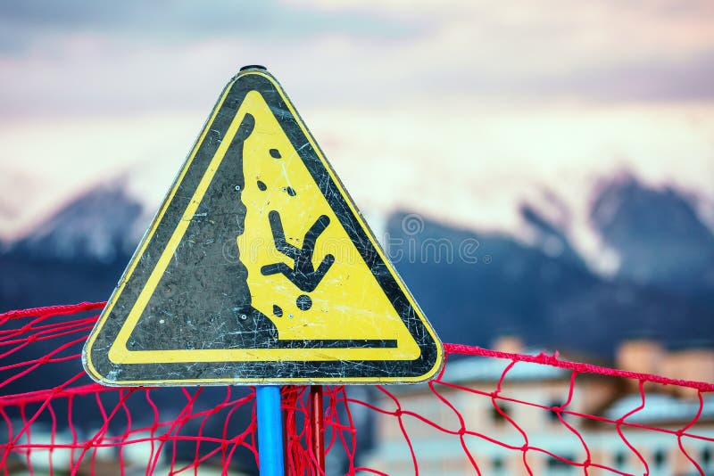 Yellow triangle outdoor warning sign on snowy mountain peaks winter background displaying man falling down a steep as safety peril