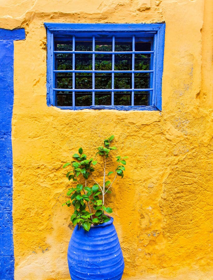 Yellow wall with blue window and pot plant in the old street on Greece. Greek style