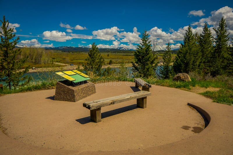 YELLOWSTONE, MONTANA, ETATS-UNIS LE 24 MAI 2018 : Belle vue extérieure de signe instructif et de chaise publique en bois avec une images stock YELLOWSTONE, MONTANA, ETATS-UNIS LE 24 MAI 2018 : Belle vue extérieure de signe instructif et de chaise publique en bois avec une images stock