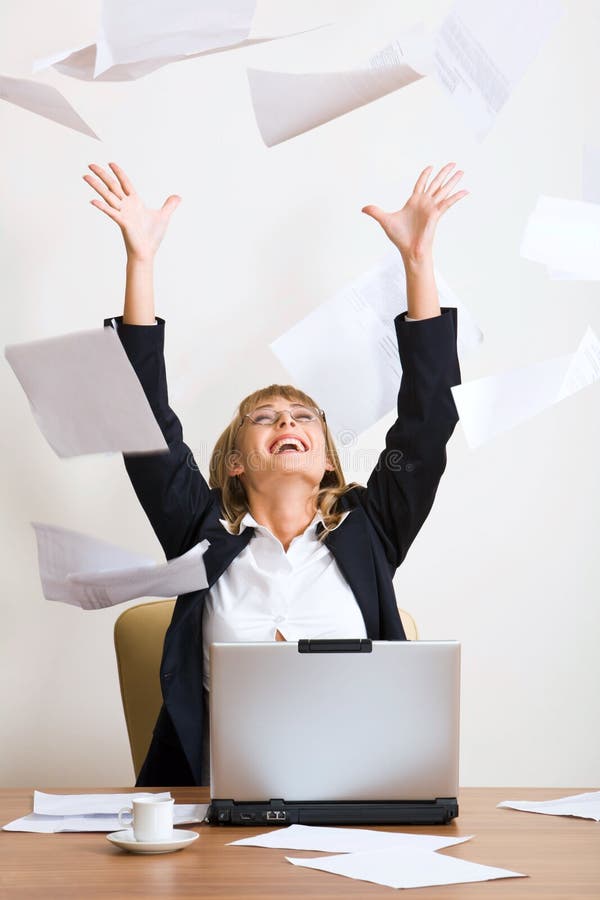 Portrait of laughing businesswoman throwing up of paper with sitting at the table with the opened laptop and a white cup on it. Portrait of laughing businesswoman throwing up of paper with sitting at the table with the opened laptop and a white cup on it