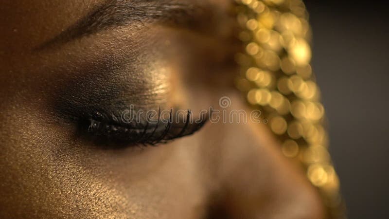 Yeux ouverts et fermés avec les fards à paupières en bronze et plots réflectorisés sur le visage de la fille africaine portant le