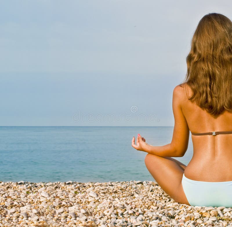 Young attractive brunette woman in swim suit doing yoga moves or meditating on sea beach