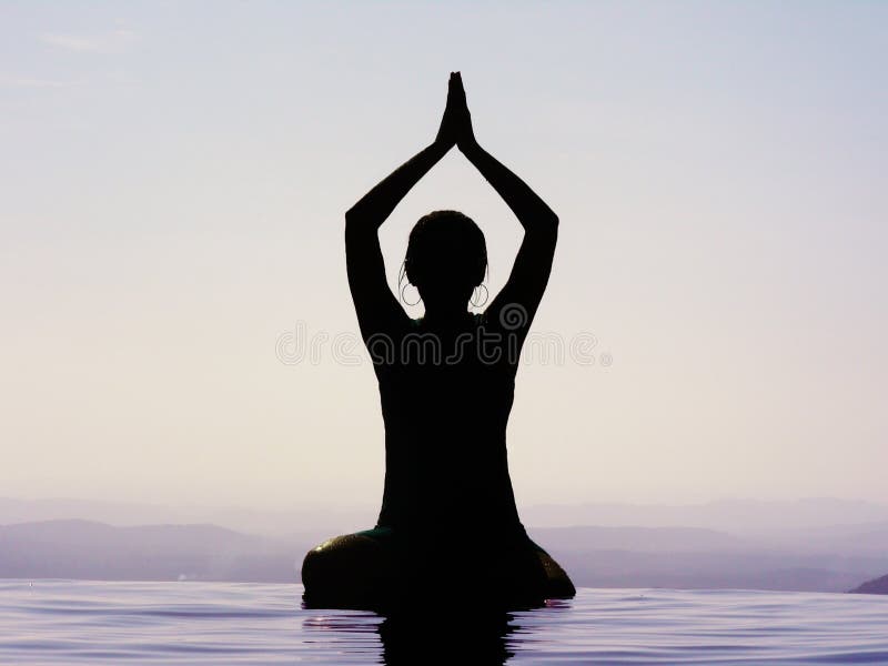 A silhouette of a woman doing yoga in water, during the early hours.