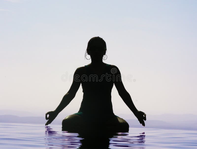 A silhouette of a woman doing yoga in water, during the early hours.