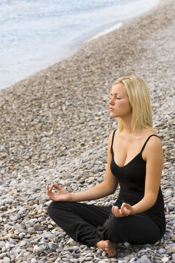 Una bella e giovane donna bionda, seduta a gambe incrociate in una posizione yoga sulla spiaggia.