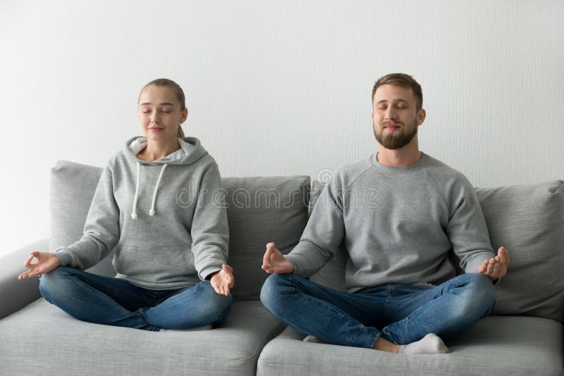 Yoga de pratique méditant de couples de calme sur le divan ensemble photo stock Yoga de pratique méditant de couples de calme sur le divan ensemble photo stock