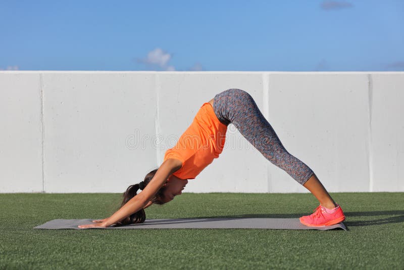 Yoga fitness woman stretching doing morning practice on exercise mat at outdoor park. Girl doing leg stretch with downward facing