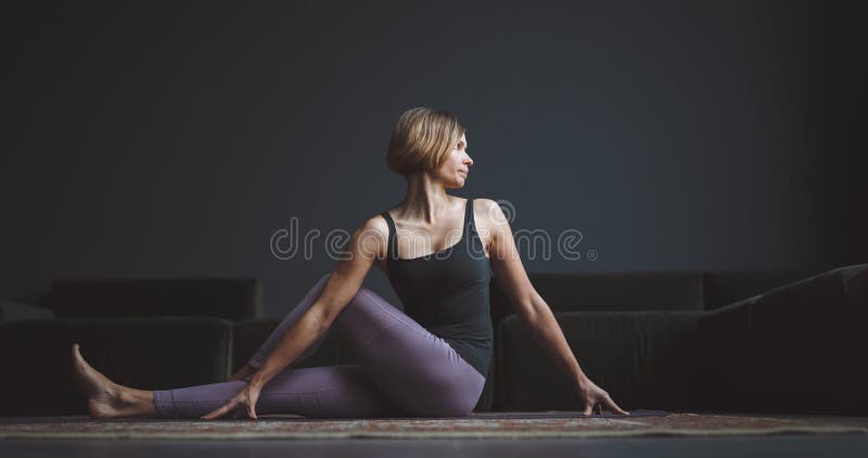 Yoga, klass. ett vackert tränat organ. en kvinna gör en asana mot en mörk bakgrund i en lägenhet i en stad. kroppens skönhet royaltyfri foto