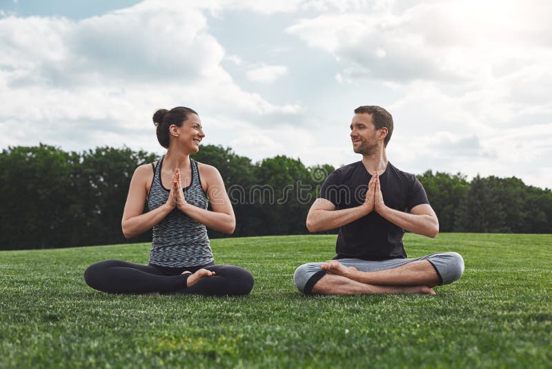 Yoga nelle paia Esercizi di pratica di meditazione delle coppie felici all'aperto ed esaminandose con il sorriso mentre sedendosi immagine stock Yoga nelle paia Esercizi di pratica di meditazione delle coppie felici all'aperto ed esaminandose con il sorriso mentre sedendosi immagine stock