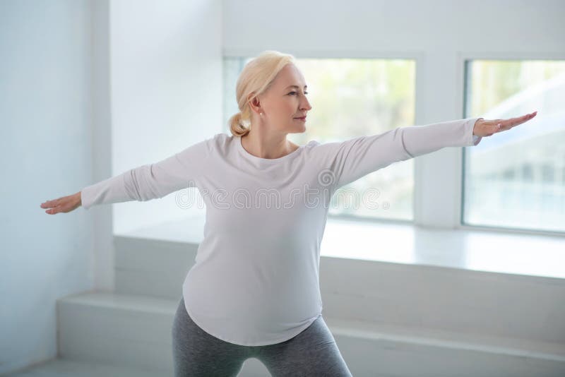 Yoga practice. Mature blonde female standing in warrior pose with arms parallel to the floor
