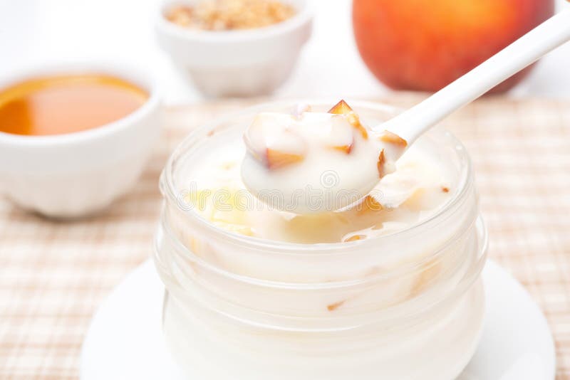 Yoghurt with honey, fresh peaches, nuts in a spoon