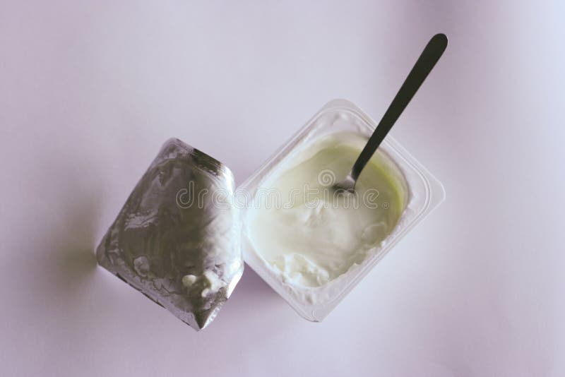 Obyčajný yougurt v plastovom môže lyžicou v ňom na neutrálnom pozadí.