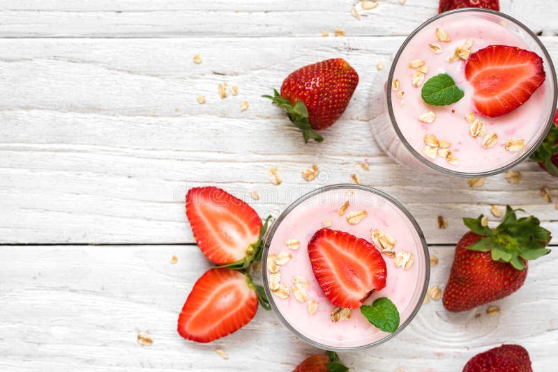 Yogurt sano della fragola con l'avena e la menta in vetri con le bacche fresche sopra la tavola di legno bianca immagine stock Yogurt sano della fragola con l'avena e la menta in vetri con le bacche fresche sopra la tavola di legno bianca immagine stock