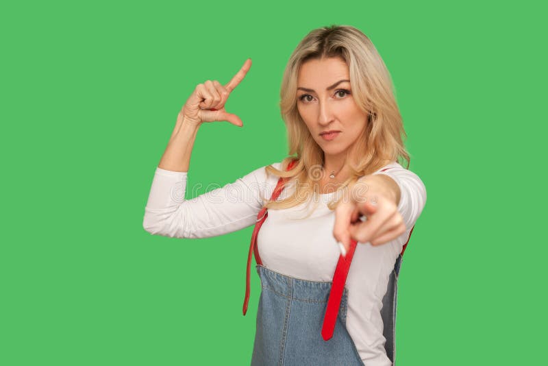 You lost job! Portrait of bossy adult woman in denim overalls showing loser gesture, pointing to camera