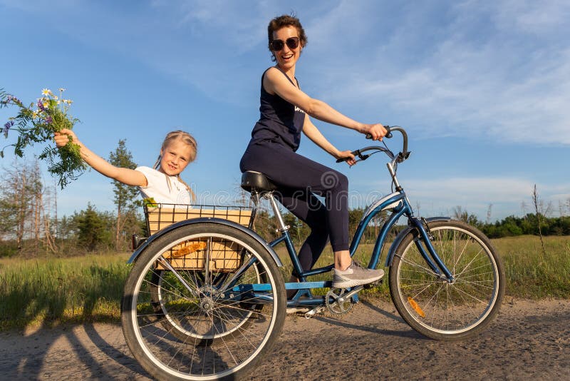 Young adult caucasian mom enjoy having leisure fun riding bicycle with cute adorable blond daughter holding wild field