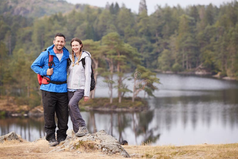 Young adult couple standing on a rock beside a lake in countryside, smiling to camera, full length stock images Young adult couple standing on a rock beside a lake in countryside, smiling to camera, full length stock images