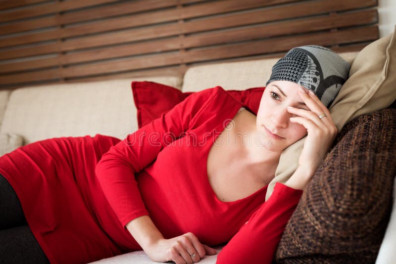 Young adult female cancer patient relaxing on a couch, watching television. Tired, depressed cancer patient. royalty free stock image Young adult female cancer patient relaxing on a couch, watching television. Tired, depressed cancer patient. royalty free stock image