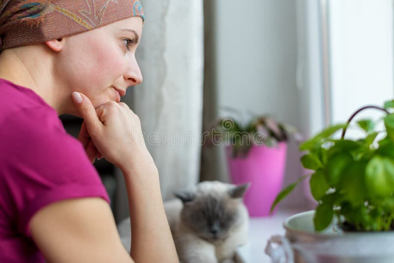 Young adult female cancer patient wearing headscarf and bathrobe sitting in the kitchen with her pet cat. royalty free stock photography Young adult female cancer patient wearing headscarf and bathrobe sitting in the kitchen with her pet cat. royalty free stock photography
