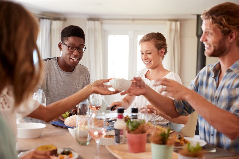 Young adult friends passing a dish across the dinner table at lunch, close up