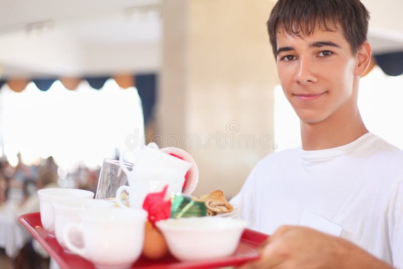 Young affable waiter keeps tray at restaurant