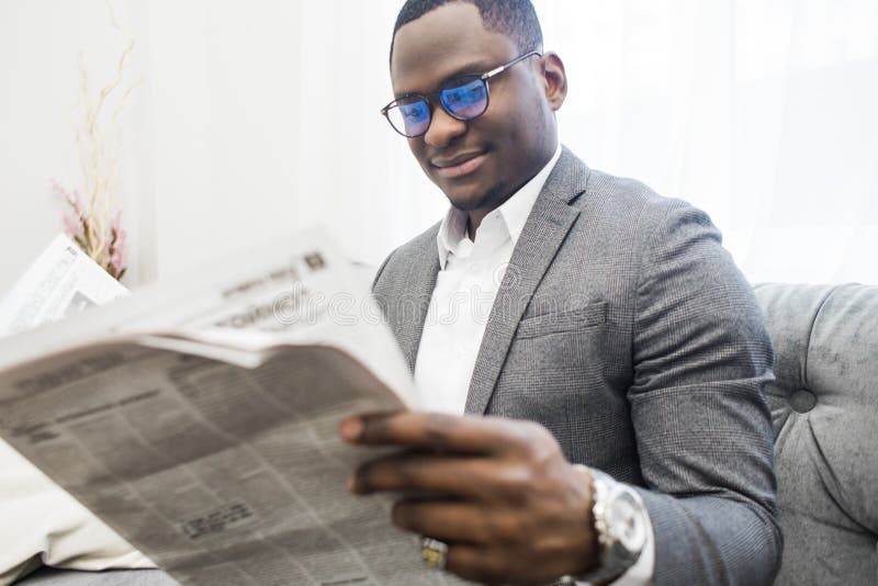 Young African American businessman in a gray suit reading a newspaper while sitting on a sofa. stock photography Young African American businessman in a gray suit reading a newspaper while sitting on a sofa. stock photography