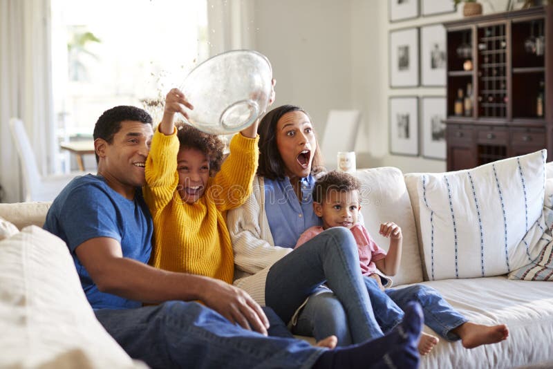 Young mixed race family sitting together on the sofa in their living room watching a scary movie. Young mixed race family sitting together on the sofa in their living room watching a scary movie