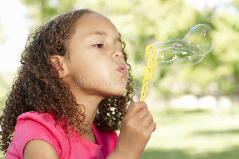 Young African American Girl Blowing Bubbles In Park royalty free stock photos Young African American Girl Blowing Bubbles In Park royalty free stock photos