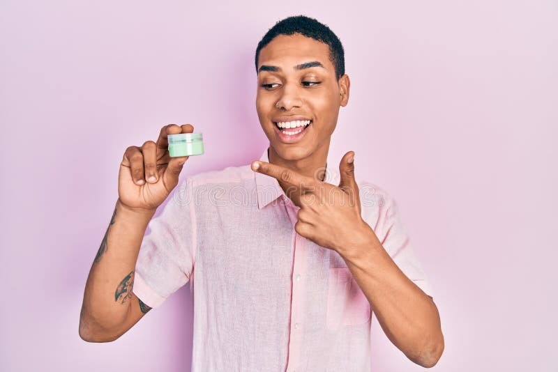 Young african american guy holding face moisturizer cream smiling happy pointing with hand and finger stock photos